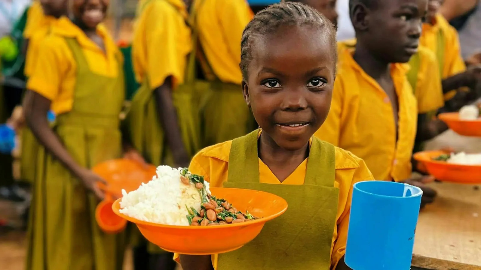 A schoolgirl holding a plate of rice and beans at a partner school-meal program